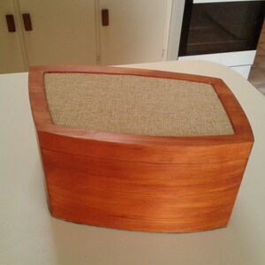 May include: A wooden box with a curved top and a fabric-covered lid. The box is a rich reddish-brown colour and has a natural wood grain.