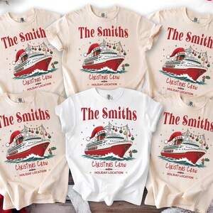 Puede incluir: Un grupo de cinco camisetas de manga corta en color crema y blanco, cada una con un gr&aacute;fico de un crucero rojo y blanco con un gorro de Pap&aacute; Noel. El texto dice The Smiths, Christmas Crew y Holiday Location, con 2026 en la chimenea.