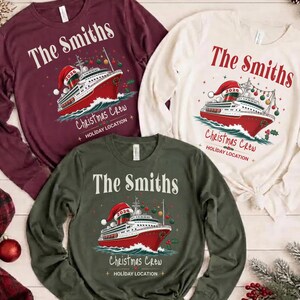 Puede incluir: Tres camisetas de manga larga en color granate, crema y verde oliva, cada una con un gr&aacute;fico de un crucero con un gorro de Pap&aacute; Noel y el texto The Smiths, Christmas Crew y Holiday Location impreso en un dise&ntilde;o festivo.