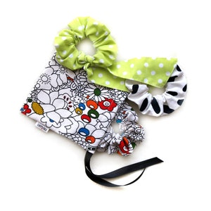 Pode incluir: Um conjunto de três scrunchies de cabelo coloridos numa bolsa de cordão com padrão floral. Os scrunchies são feitos de tecido e têm um aspeto franzido. A bolsa é branca com um padrão floral preto e colorido. A bolsa tem um cordão de ajuste preto e uma etiqueta que diz "notion".