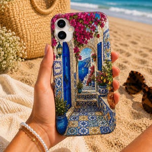 Può includere: Una cover per smartphone con una vivace scena mediterranea che mostra una porta blu, fiori di bouganville rosa e piastrelle decorate. L'illustrazione raffigura una vista costiera con il mare, una barca a vela e piante in vaso in stile mosaico.