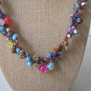May include: A colorful beaded necklace with a brown cord. The necklace features a variety of beads in shades of pink, blue, yellow, and brown. The beads are of different shapes and sizes, creating a unique and eye-catching design.