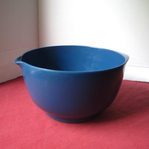 May include: A deep blue mixing bowl with a smooth matte finish, featuring a rounded body and a small integrated pouring spout on one side. The bowl has a wide circular opening and a stable base, designed for kitchen use and food preparation.