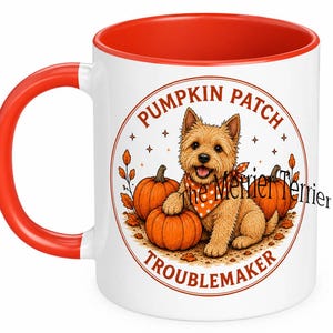 Puede incluir: Una taza de cerámica blanca con asa y borde interior de color rojo brillante. El frente presenta un gráfico circular de un terrier color canela con un pañuelo naranja de lunares, rodeado de calabazas y hojas de otoño, con el texto PUMPKIN PATCH TROUBLEMAKER.