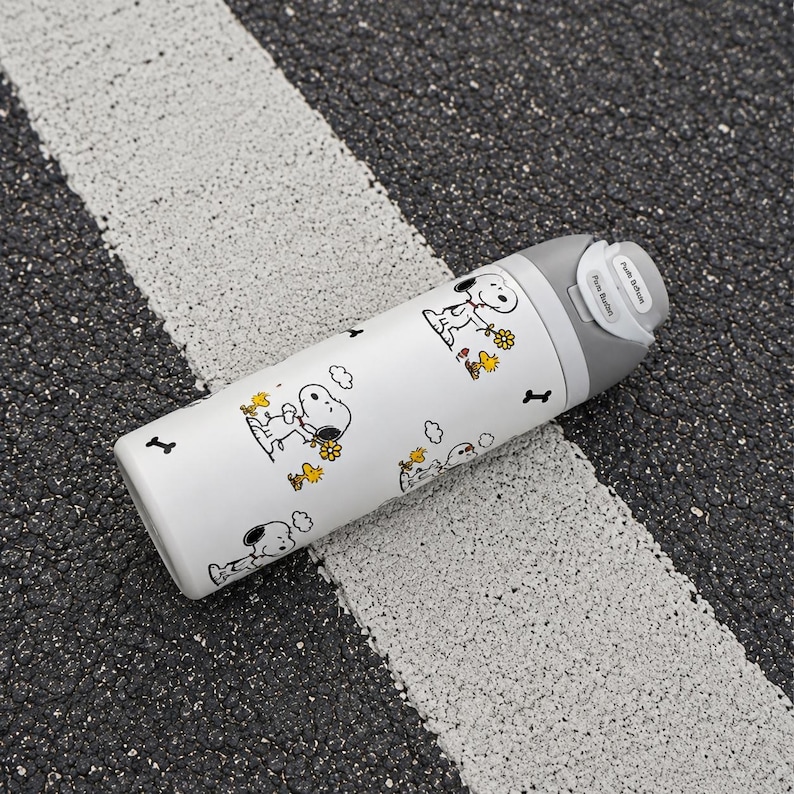 Puede incluir: Botella de agua blanca con un patr&oacute;n repetido de ilustraciones de Snoopy con flores y nubes. La botella tiene una tapa gris con un bot&oacute;n y un icono de hueso de perro en blanco y negro. La botella est&aacute; sobre una superficie en blanco y negro.