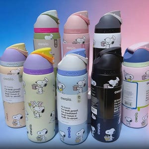 May include: A collection of Owala insulated water bottles in various colors, including pink, blue, and black. Each bottle features a Snoopy cartoon design and the text "owala". The bottles have built-in straws and are leak-proof.