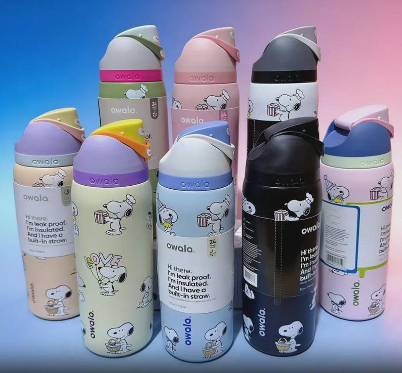 May include: A collection of Owala insulated water bottles in various colors, including pink, blue, and black. Each bottle features a Snoopy cartoon design and the text "owala". The bottles have built-in straws and are leak-proof.