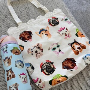 Pu&ograve; includere: Una borsa tote in tela bianca con bordo superiore smerlato e una borraccia azzurra, entrambe caratterizzate da un motivo ripetuto di varie razze canine che indossano cappelli, occhiali e cuffie colorati, con il testo Good Boy 777 su un cane.