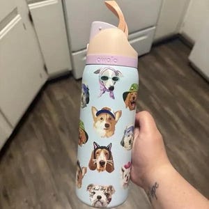 Pu&ograve; includere: Una borraccia Owala azzurra con vari ritratti illustrati di cani che indossano accessori come cappelli e occhiali da sole. La bottiglia ha un manico color pesca e un coperchio color lavanda. I cani sono raffigurati in vari stili.