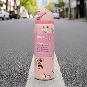 Puede incluir: Una botella de agua aislada Owala rosa con un dise&ntilde;o de Snoopy. La botella tiene una pajita incorporada y es a prueba de fugas. La botella tiene el texto "Hi there. I'm leak proof. I'm insulated. And I have a built-in straw."