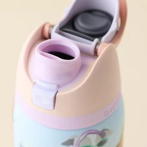 Pu&ograve; includere: Una borraccia azzurra con coperchio color pesca e beccuccio color lavanda. Il coperchio &egrave; aperto e rivela una guarnizione in silicone grigio scuro. La bottiglia presenta una stampa grafica di un cane con un foulard viola e occhiali da sole verdi.