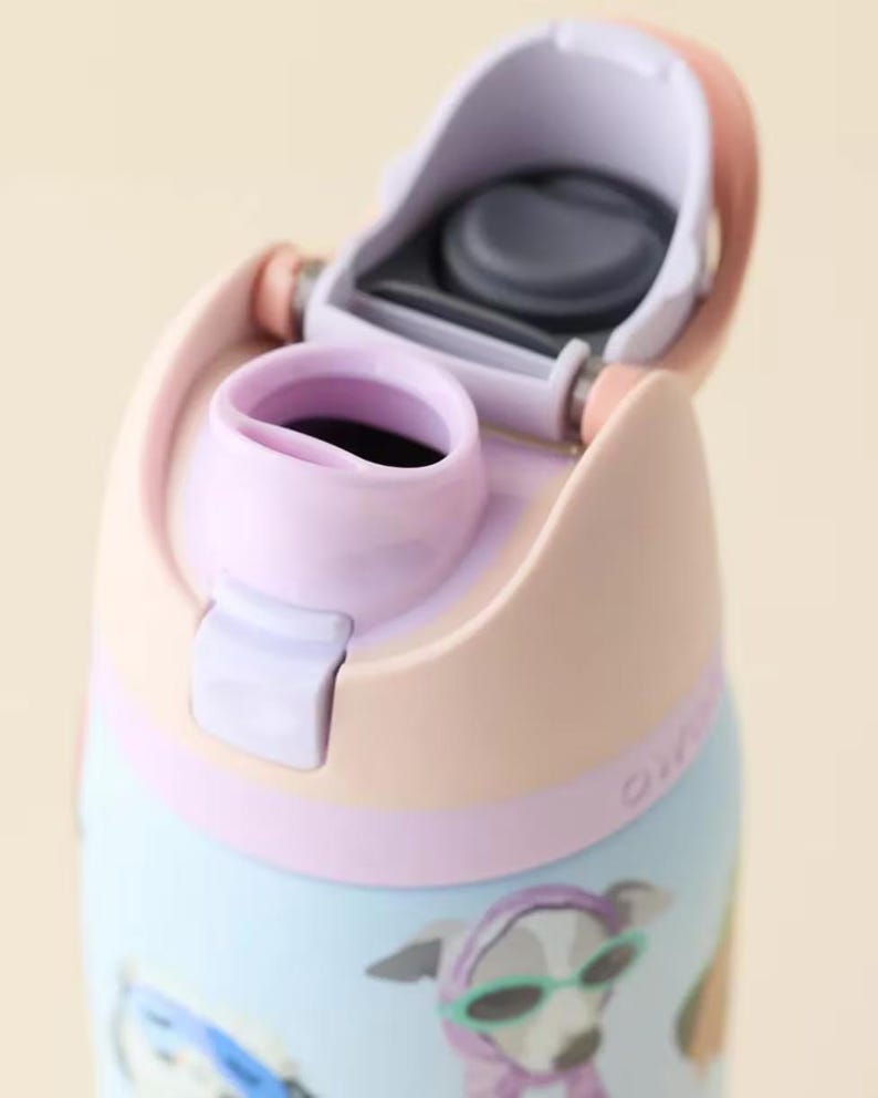 Pu&ograve; includere: Una borraccia azzurra con coperchio color pesca e beccuccio color lavanda. Il coperchio &egrave; aperto e rivela una guarnizione in silicone grigio scuro. La bottiglia presenta una stampa grafica di un cane con un foulard viola e occhiali da sole verdi.