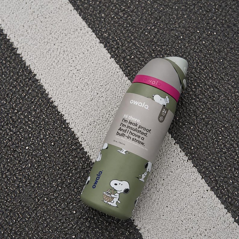 Puede incluir: Una botella de agua Owala verde oliva con un dise&ntilde;o de dibujos animados de Snoopy. La botella tiene una tapa gris y una banda rosa. El texto en la botella dice: "Hola. Soy a prueba de fugas. Estoy aislado. Y tengo una pajita incorporada." Capacidad: 946 ml.