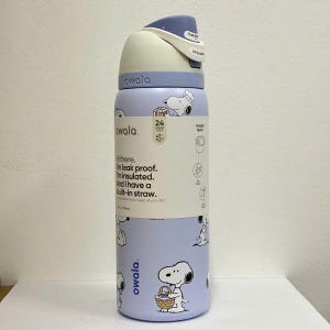May include: A light purple Owala water bottle with a Snoopy pattern. The bottle has a white and blue lid with a push-button opening. The bottle has a built-in straw and is insulated. The bottle is 9.5 inches tall and holds 24 ounces.