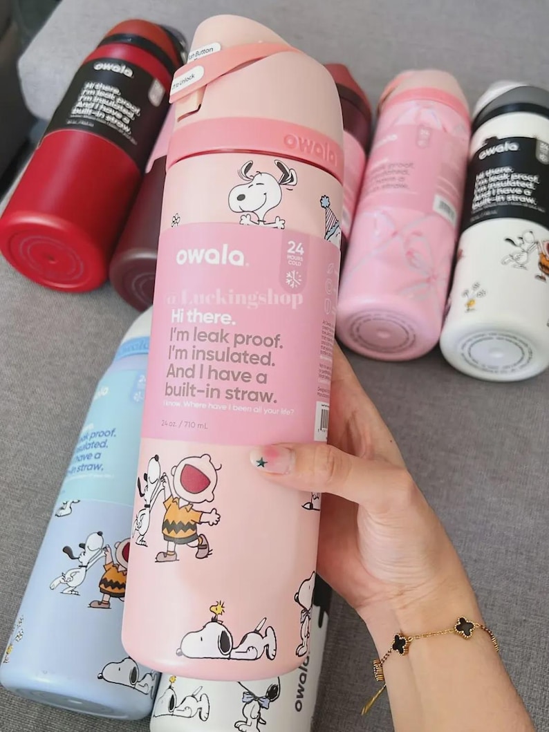 May include: Pink Owala water bottle with Snoopy and Charlie Brown graphics. The bottle has a built-in straw and is leak-proof. The bottle is 24 oz / 710 ml.