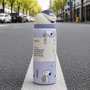 Puede incluir: Una botella de agua Owala de color lila claro con ilustraciones de Snoopy. La botella tiene una tapa blanca y morada con apertura de bot&oacute;n. El texto en la botella dice: "Hola. Soy a prueba de fugas. Estoy aislado. Y tengo una pajita incorporada."