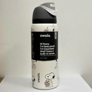 May include: A white Owala insulated water bottle with a black and gray lid. The bottle features a repeating Snoopy design and text that reads, "Hi there. I'm leak proof. I'm insulated. And I have a built-in straw." It holds 32 oz.