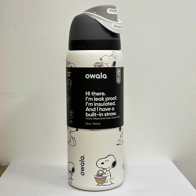 May include: A white Owala insulated water bottle with a black and gray lid. The bottle features a repeating Snoopy design and text that reads, "Hi there. I'm leak proof. I'm insulated. And I have a built-in straw." It holds 32 oz.