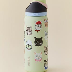May include: A light green Owala water bottle featuring a repeating pattern of various cat illustrations, including cats wearing accessories like a red beret, a pink bow, and a spa face mask. The bottle has a black, light blue, and pale green lid.