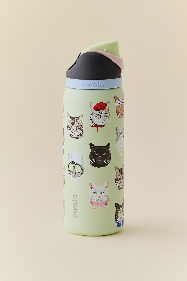 May include: A light green Owala water bottle featuring a repeating pattern of various cat illustrations, including cats wearing accessories like a red beret, a pink bow, and a spa face mask. The bottle has a black, light blue, and pale green lid.