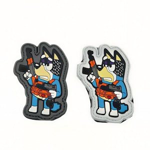 May include: Two rubberised patches featuring a cartoon dog character in a blue outfit, holding a rifle and a handgun, wearing an orange tactical vest with pouches. One patch has a dark grey border, and the other has a light grey border.