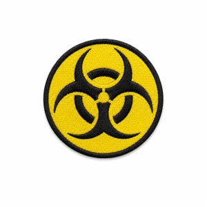 May include: A circular embroidered patch featuring a black biohazard symbol centered on a bright yellow background. The design is enclosed by a thick black stitched border, creating a high-contrast emblem with a textured fabric appearance.