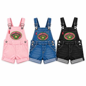 May include: Three pairs of short dungarees in pink, blue denim, and black denim. Each pair features adjustable shoulder straps with metal buckles, a front bib pocket with a Cabbage Patch Kids patch, side buttons, and cuffed hems at the legs.