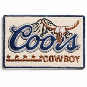 Peut inclure: Un écusson rectangulaire brodé sur fond crème avec une bordure bleu foncé. Il présente le mot Coors en écriture bleue, une silhouette de montagne, un crâne de longhorn marron et le mot COWBOY en marron avec cinq étoiles au-dessus d'une ligne.