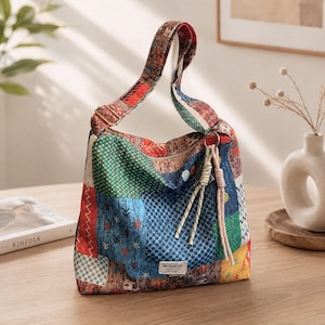 May include: A hobo bag featuring a multi-coloured patchwork design with various geometric and floral patterns in shades of red, blue, green, and yellow. The bag has a long shoulder strap, a zip closure, and a small rectangular label reading MULAIDI.