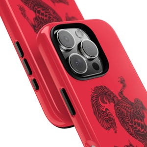 May include: Vibrant red phone case featuring a black illustration of a mythical beast. The case has a black camera lens surround and black side buttons. The phone case is shown at an angle, with a second case in the background.