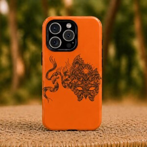 May include: Bright orange phone case with a black graphic design. The design features a detailed illustration of a mask, sun, and a serpent-like creature. The phone case has a glossy finish and a camera bump.