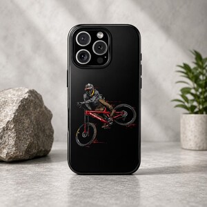 Könnte beinhalten: Schwarze Handyhülle mit einer Grafik eines Mountainbikers auf einem roten Fahrrad. Die Illustration zeigt den Biker in der Luft, in einem grau-schwarzen Outfit. Die Handyhülle hat eine glänzende Oberfläche.
