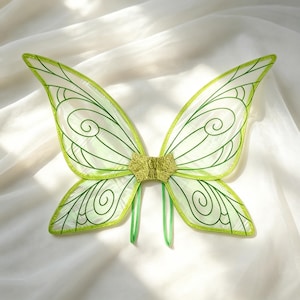May include: A pair of translucent lime green fairy wings featuring a delicate dark green vein pattern with swirling details. The wings are connected by a central textured gold-coloured piece and include two thin green straps for attachment.