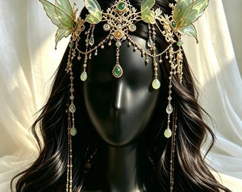 May include: A gold-toned headpiece featuring translucent pale green butterfly wings, intricate filigree metalwork, and dangling teardrop-shaped green beads. The accessory includes delicate gold chains that drape across the forehead.