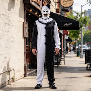 Puede incluir: Un disfraz de payaso en blanco y negro que presenta un mono de manga larga con un diseño de colores divididos, un cuello con volantes y tres grandes pompones negros en la parte delantera. El conjunto incluye una máscara de payaso blanca a juego.