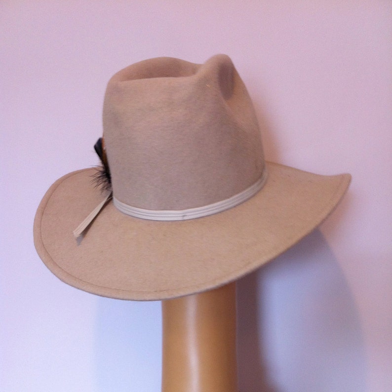 May include: A beige felt cowboy hat with a white band and a small black feather accent.