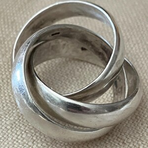 May include: A silver ring with three interlocking bands. The ring is smooth and polished.