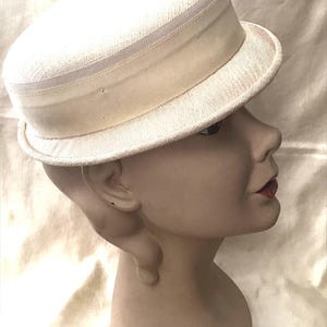 May include: A white straw hat with a wide brim and a white ribbon band. The hat has a small flower embellishment on the top.
