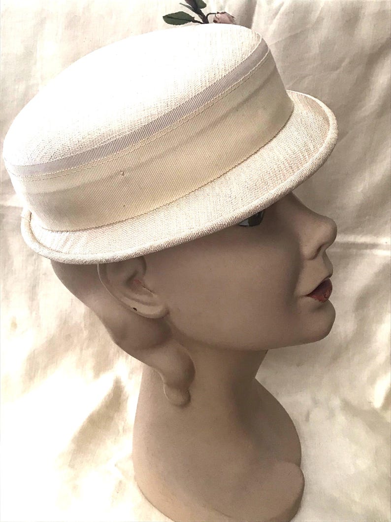 May include: A white straw hat with a wide brim and a white ribbon band. The hat has a small flower embellishment on the top.