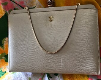 May include: A beige leather clutch purse with a gold chain strap and a decorative clasp. The purse has a subtle textured pattern.