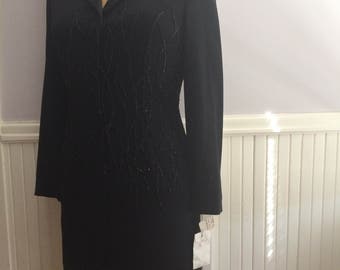 May include: A black long-sleeved dress with a beaded design on the front. The dress has a collar and a fitted silhouette.