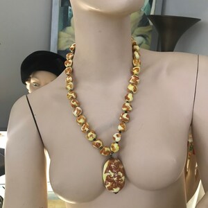 May include: A yellow and brown ceramic necklace with a large pendant. The pendant is oval shaped and has a detailed design.