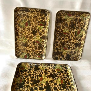 May include: Three rectangular metal trays featuring a dense, repeating pattern of dark brown floral silhouettes, small red rose blossoms, and green leaves set against a muted yellow background. Each tray has rounded corners and a shallow, raised rim.