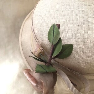 May include: A beige hat with a wide brim and a pink rose with green leaves attached to the side.