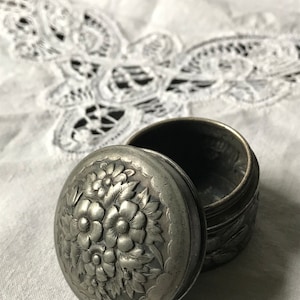May include: A silver trinket box with a floral design on the lid. The box is open and the inside is visible.