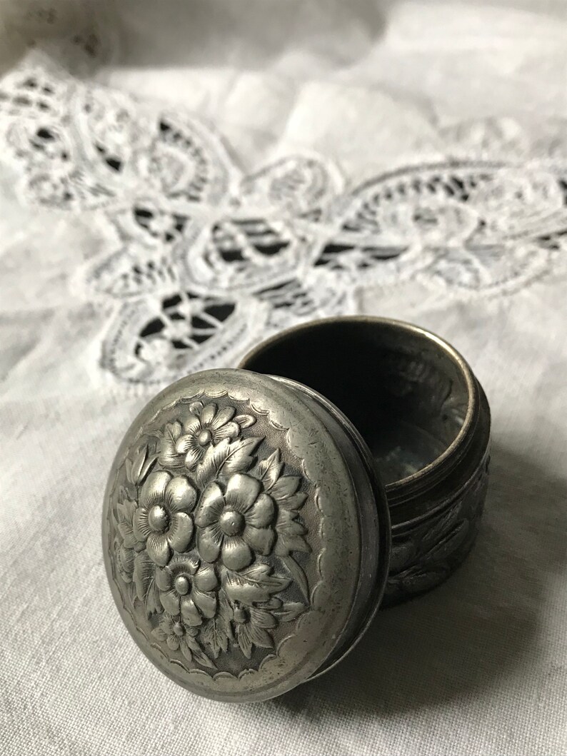 May include: A silver trinket box with a floral design on the lid. The box is open and the inside is visible.