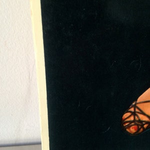 May include: A black and white image of a woman's foot wearing a black strappy sandal. The sandal has a criss-cross design and the woman's toes are painted red. The image is on a black background with the text "8430 ENTICING" at the bottom.