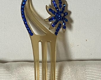 May include: A gold hair comb with three tines and a blue rhinestone flower design.
