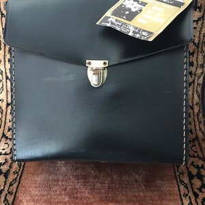May include: A black leather briefcase with a silver clasp and a white stitched border. The briefcase has a tag attached to it that reads "Nationally Distributed".