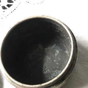 May include: A silver, round, decorative box with a slightly tarnished interior. The box has a textured, embossed design on the exterior.